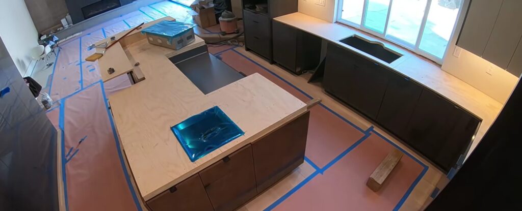 High-angle view of a modern kitchen under construction with plywood templates on the island and protective paper on the floors.