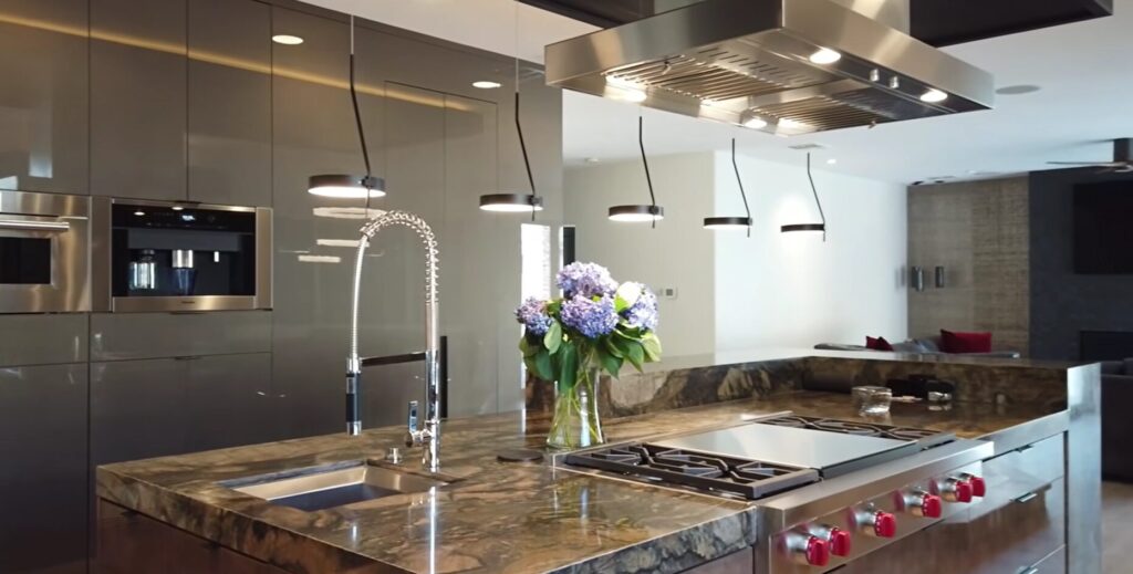 A finished high-end kitchen with dark marble countertops, a professional range, modern pendant lighting, and a bouquet of purple hydrangeas.