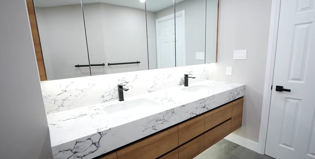 A sleek bathroom featuring a long marble countertop with two white sinks, black faucets, and a large multi-paneled mirror.